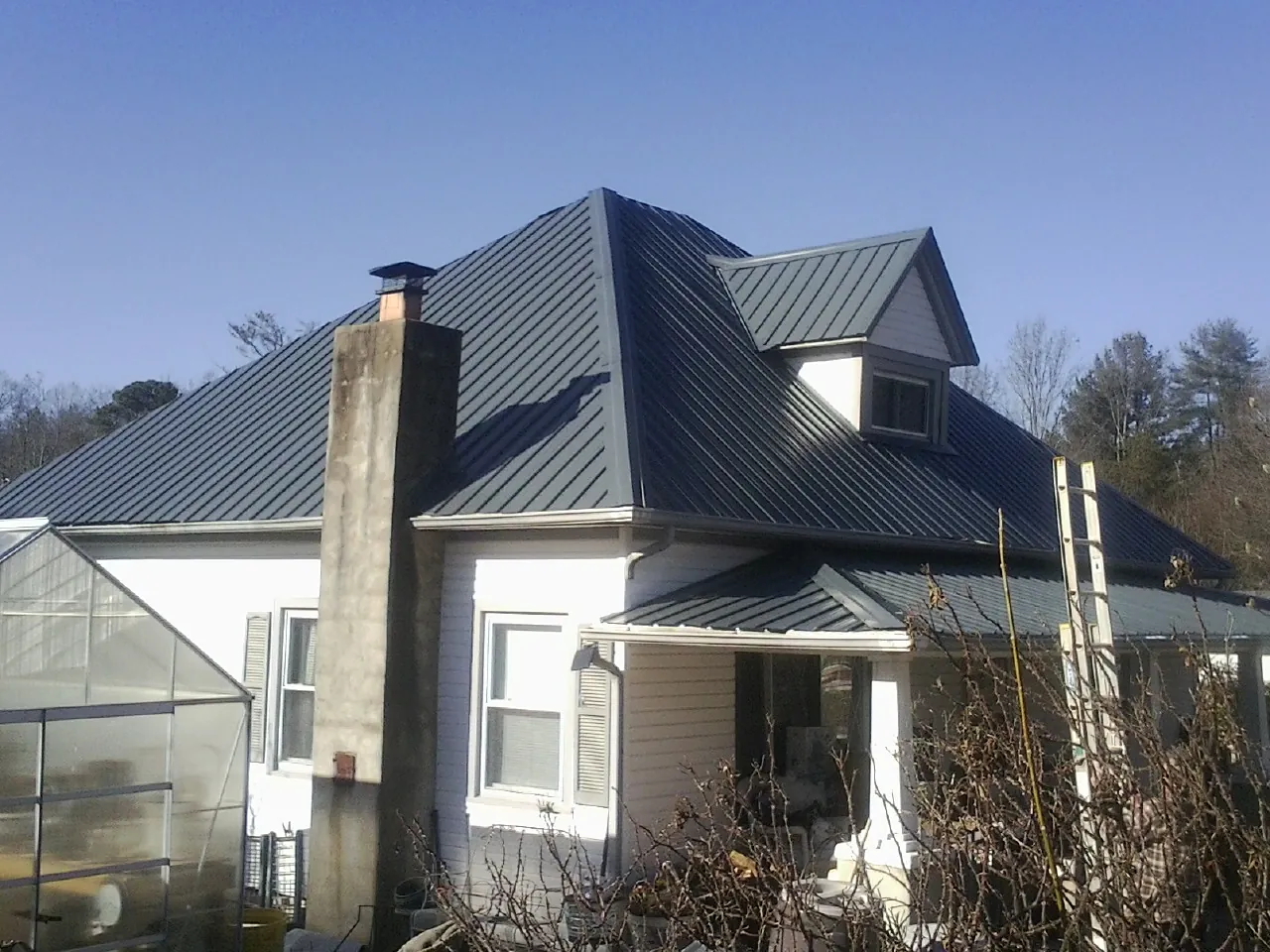 Dark blue standing seam metal roof on a white farmhouse with dormer — Slate & Tile Roof Repair by Roofing Brothers in Gulf Breeze