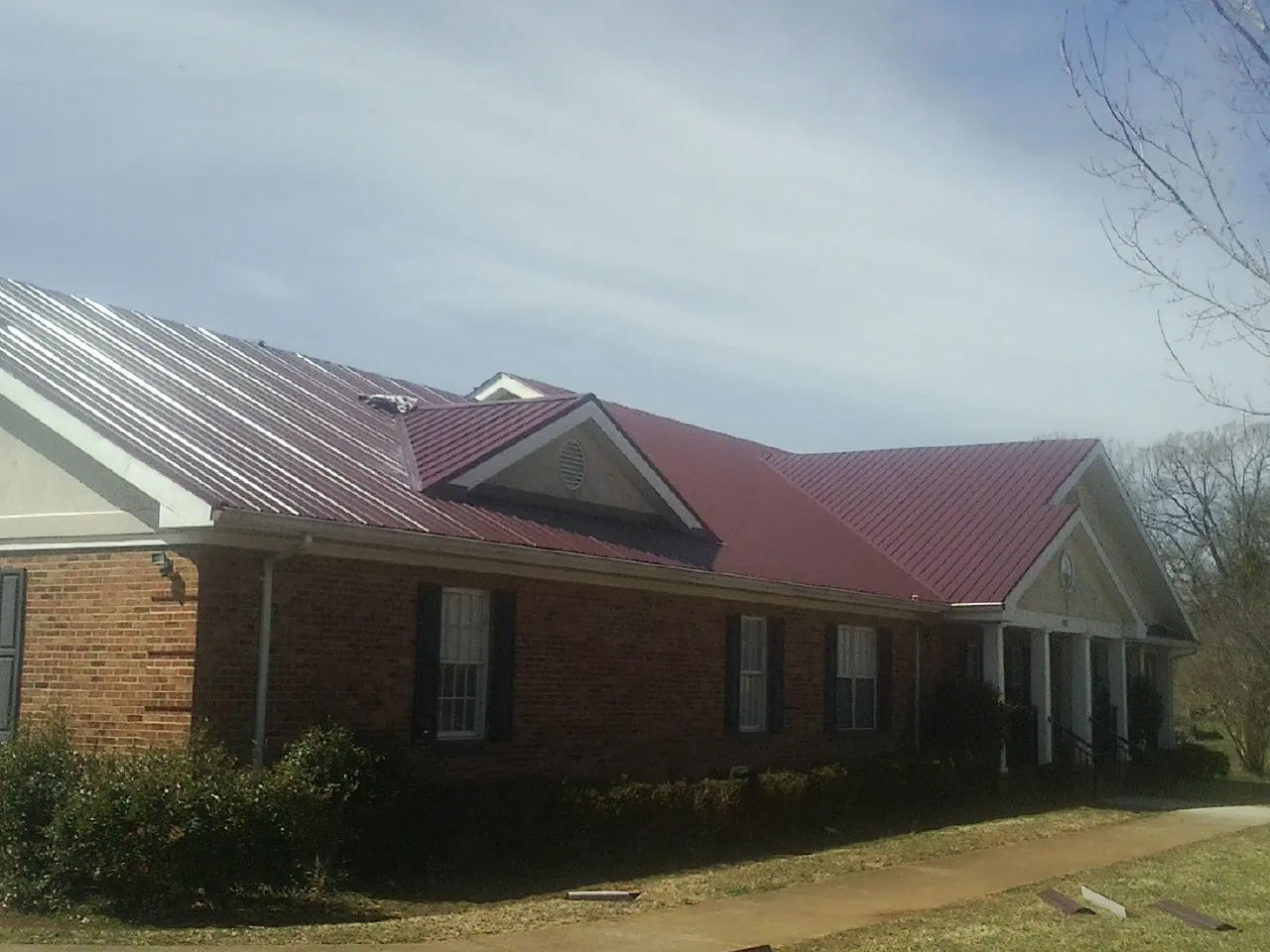 Red metal roof with gabled entries on a long brick building, from a Hail Damage Roof Repair job in Gulf Breeze
