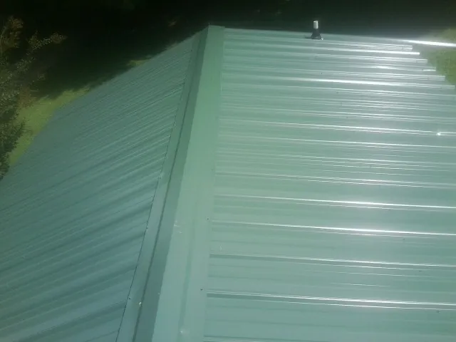 New green metal panels meeting at the ridge of a roof — Flat Roof Repair work by our crew in Gulf Breeze
