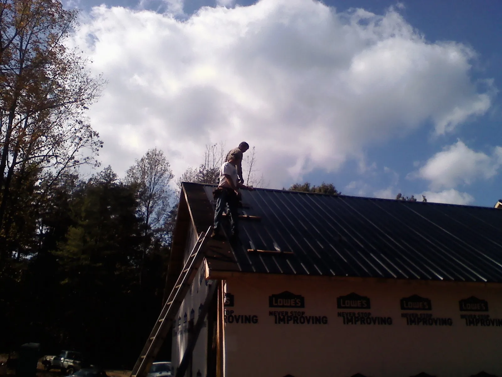 Roofer fastening dark metal panels high against a cloudy sky, from a Roof Inspection job in Gulf Breeze