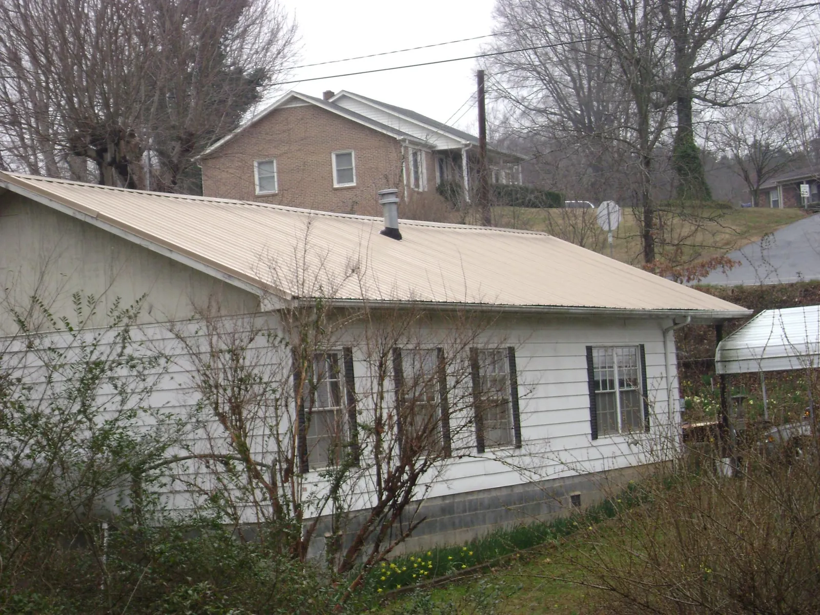 Tan metal roof on a white sided house set into a hillside — Commercial Roofing by Roofing Brothers in Gulf Breeze