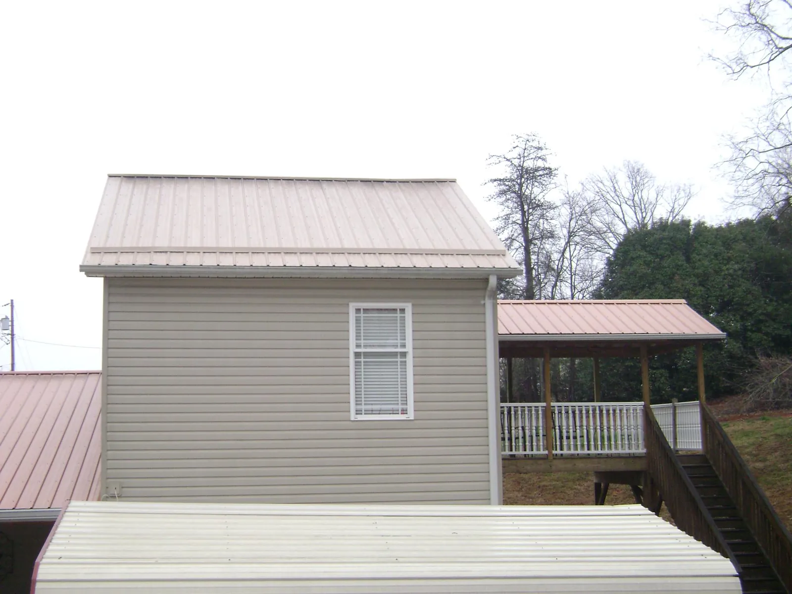 Tan metal roofs on a two story addition and attached porch, from a Roof Replacement job in Gulf Breeze